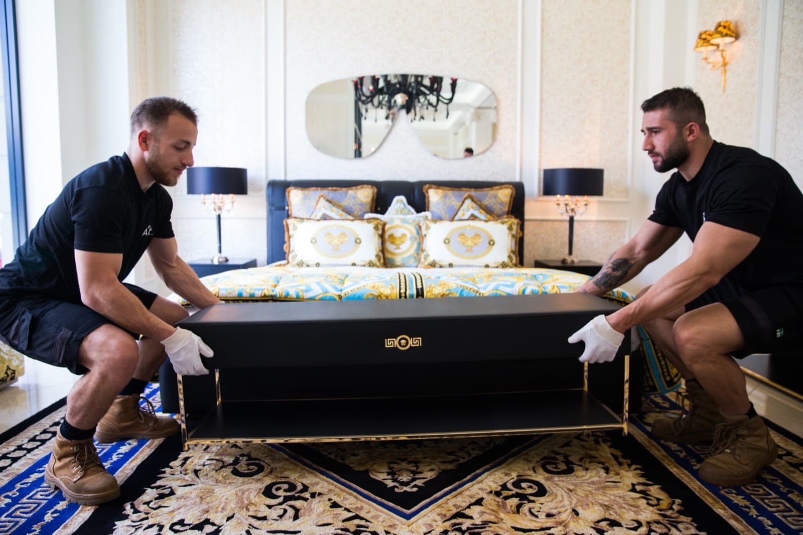 Ateam Logistics handlers lowering an ornate gilded daybed into position between two lamps in a finished room.