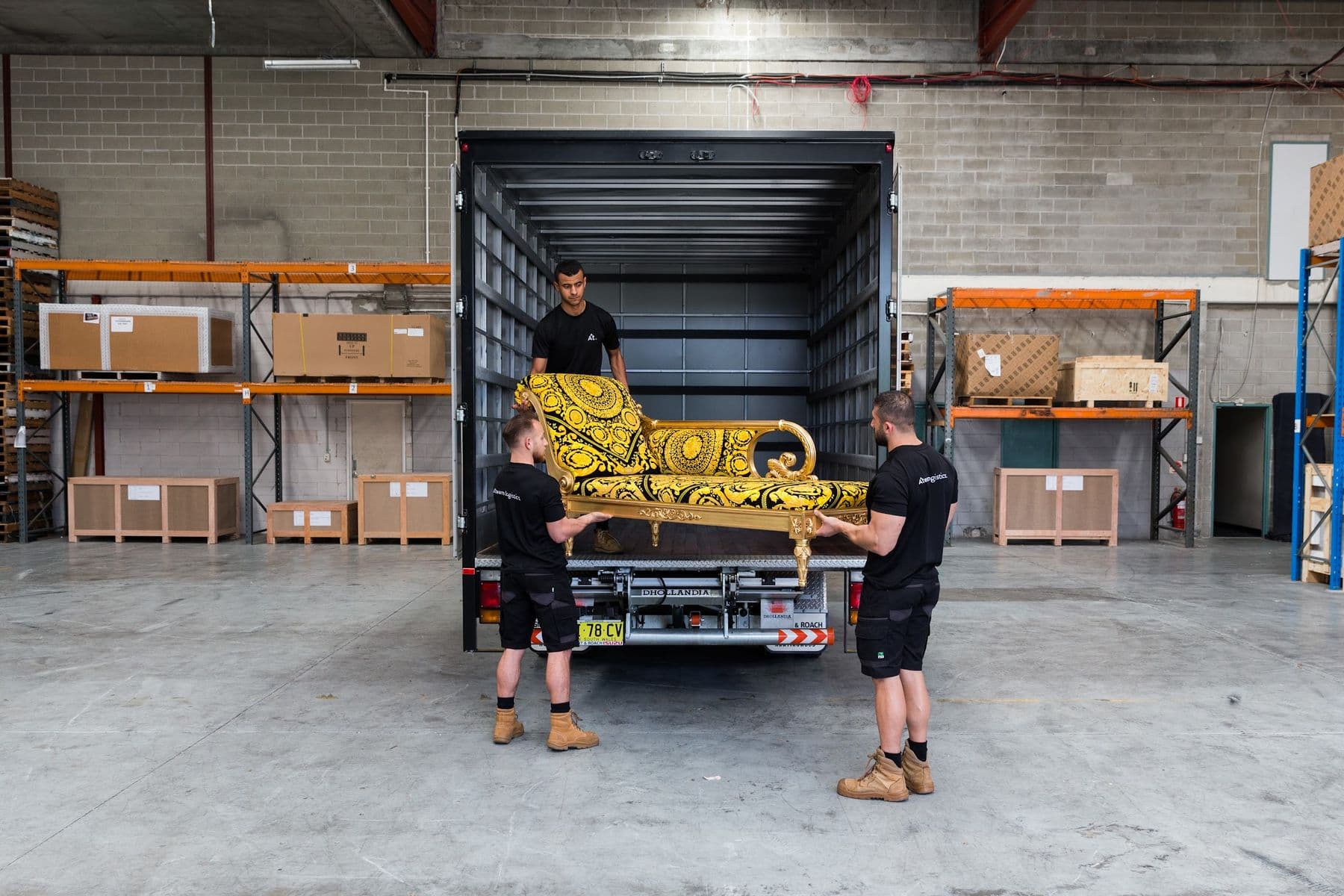 Two Ateam Logistics handlers loading an ornate chaise longue onto a truck tail lift.