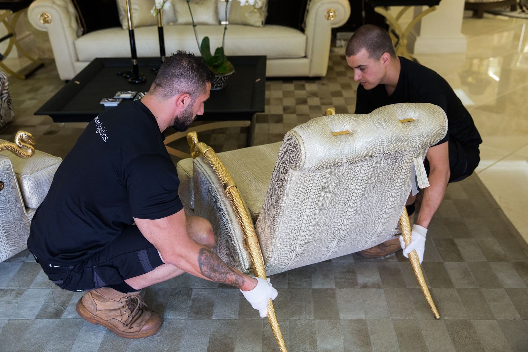 Two handlers crouching to tilt and turn an upholstered chair.