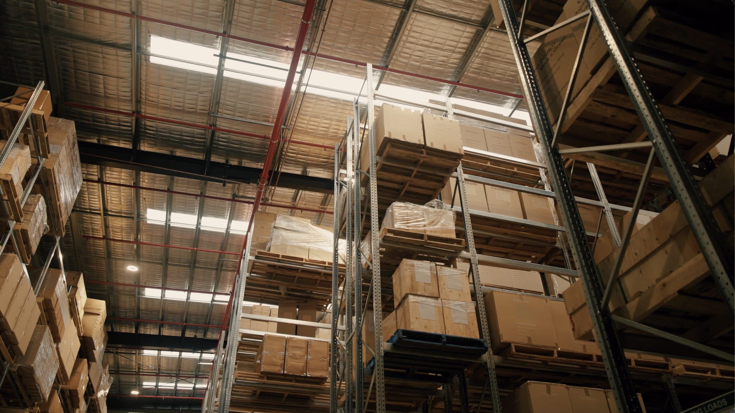 Racking inside the Ateam Logistics facility, stacked several levels high with crated and cartoned stock beneath the roof lights.