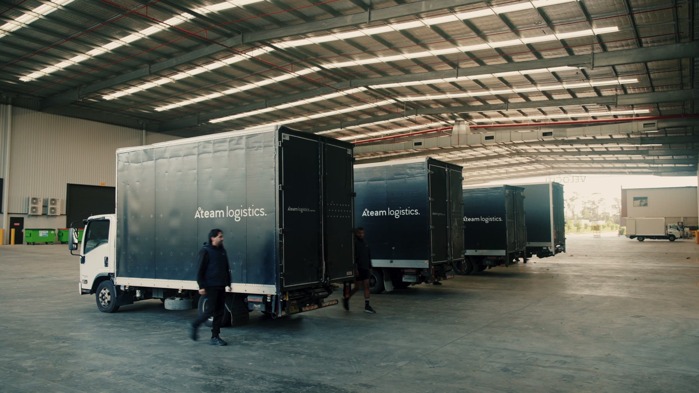 Three branded Ateam Logistics trucks in the loading bays at the depot.